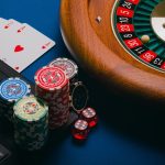 Close-up of poker chips, playing cards, and a roulette wheel on a blue table.